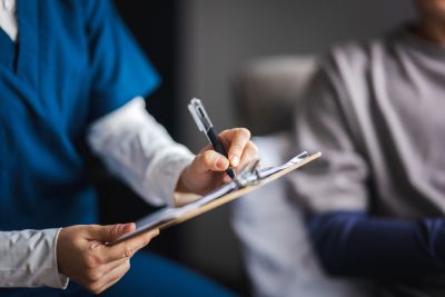 Healthcare professional taking notes on a clipboard during a patient consultation.