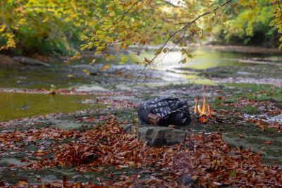 Small campfire and backpack by a river in autumn.
