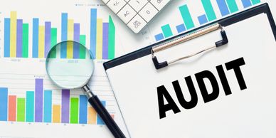 Magnifying glass, charts, and clipboard with the word AUDIT for financial review.