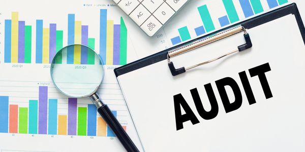 Magnifying glass over charts and clipboard with 'AUDIT' text.