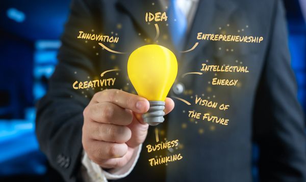 A person holding a glowing light bulb with innovation concepts around it.