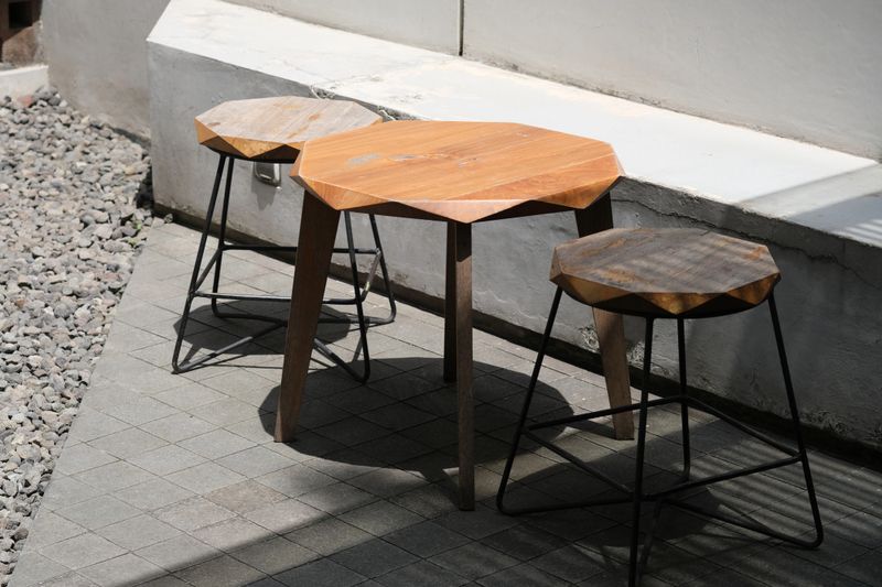 Set of wooden stools and a matching table with angular geometric tops, placed outside on a wooden deck in natural sunlight.
