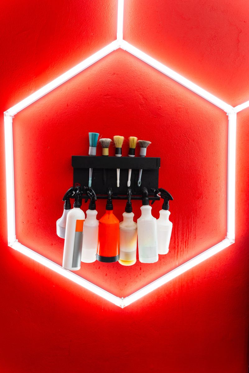 Brushes and spray bottles neatly organized for car detailing. Detailing car cleaning bottles and brushes aligned neatly against neon lighting