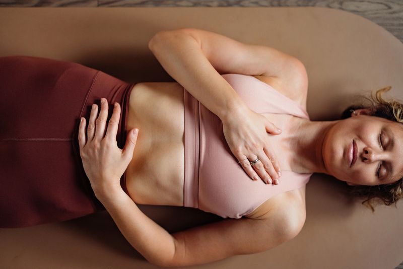 A calm woman rests on a yoga mat in a soft pink top, hands over her chest. This stock image conveys wellness, mindfulness, fitness, relaxation, and focus for yoga or wellness campaigns.