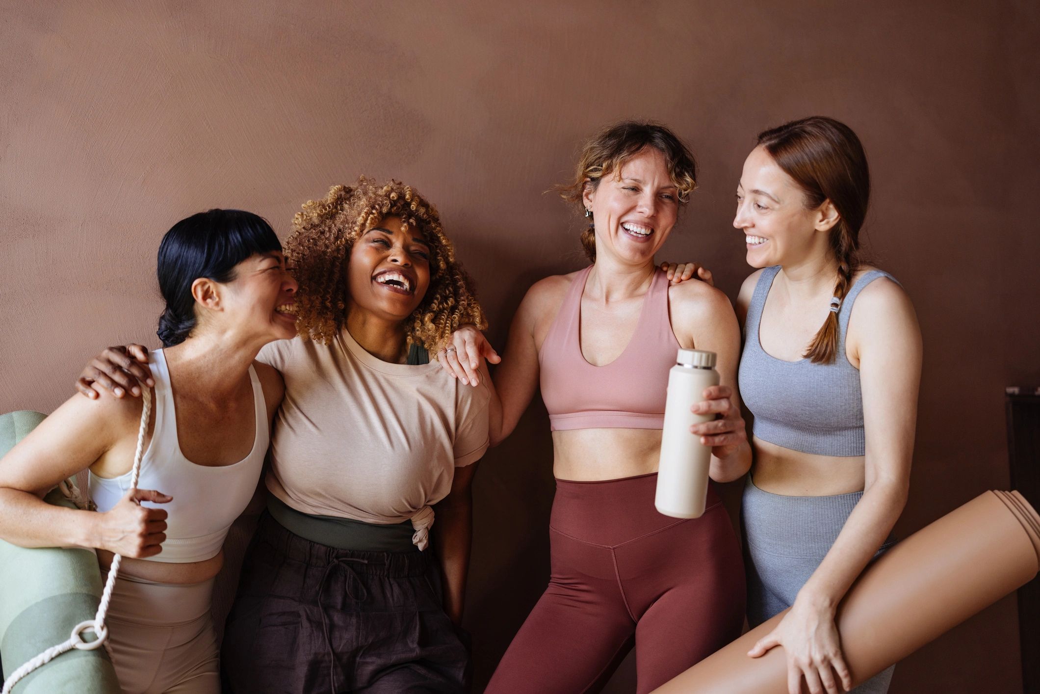 Four women in workout clothes laughing together.