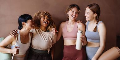 Four women in workout gear smiling and hugging.