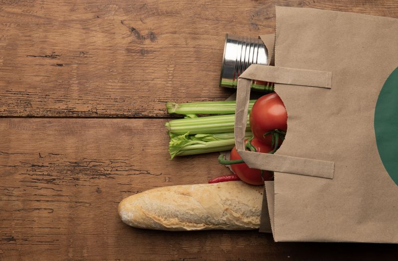 Paper bag with tomatoes, celery, chili pepper and baguette on rustic wooden background. Concept of zero waste shopping, local organic food and sustainable lifestyle.