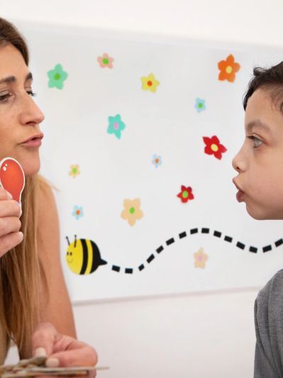 A woman helps a boy with speech exercises using flashcards.