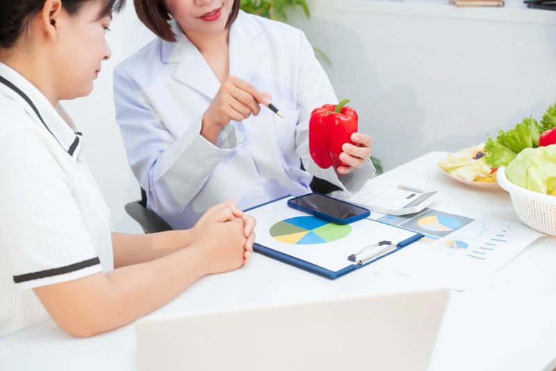 Professional Asian female nutritionist giving nutritional counseling to female patient sitting at clinic table discussing diet, health goals, meal plans and strategies for long-term wellness