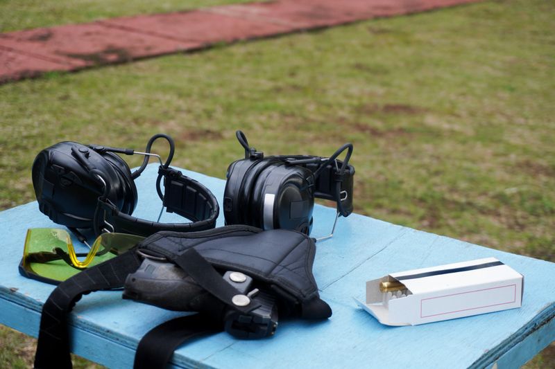 Gear ready for target practice: headphones, safety glasses, and ammunition box sit on a blue table at the shooting range.