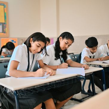 Students in uniform focused on writing at their desks in a classroom.