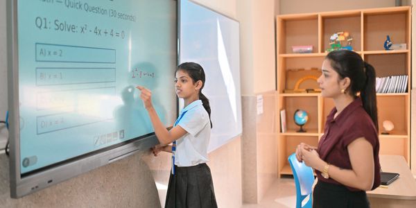 Student solving a quadratic equation on a smart board with a teacher watching.