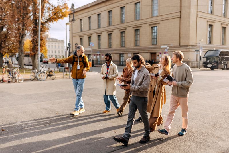 Group of friends with a travel guide walking on a street  near the classical columns at Museum Island in Berlin, enjoying sightseeing, cultural exploration, and a relaxed travel experience