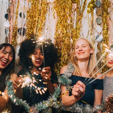 Four women joyfully holding sparklers at a festive party with glittering decorations.
