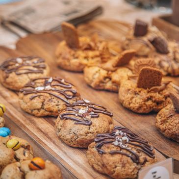 Assorted gourmet cookies with chocolate drizzle and toppings on wooden trays.