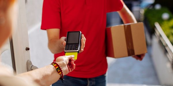 Delivery person in red offering card payment for package at doorstep.