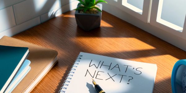 Notebook with 'WHAT'S NEXT?' written on it and a fountain pen on a wooden desk.