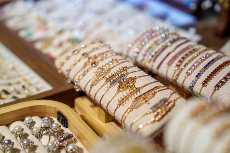 A close-up view of assorted gold and gemstone bracelets arranged neatly on a display cushion in a jewelry shop. The colorful stones, metal details, and elegant craftsmanship highlight the beauty and luxury of the accessories.