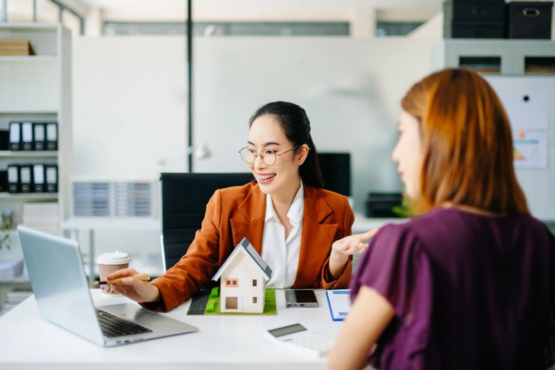 Smiling real estate agent showing calculator to client with house model. Perfect for property consultation, mortgage deal, finance, and investment planning themes.