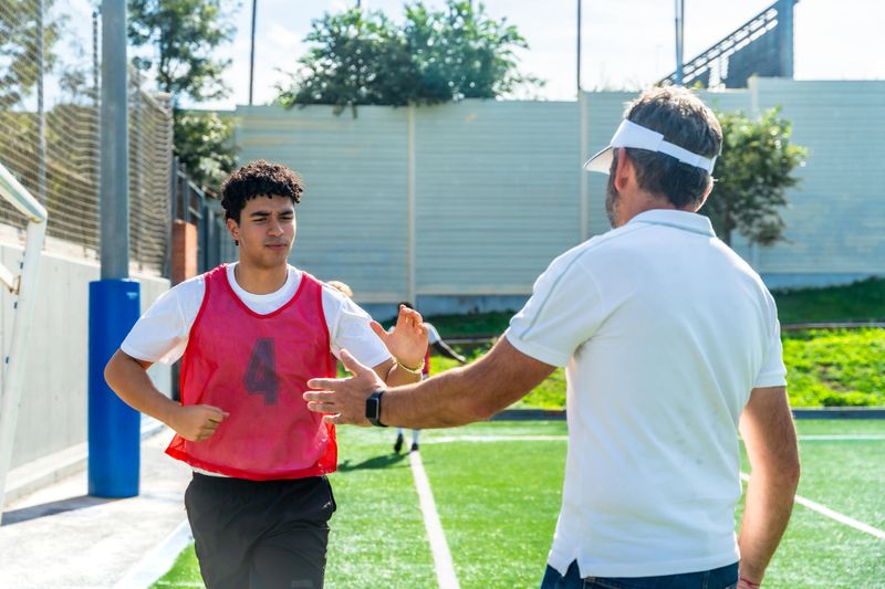 Soccer coach giving a high five to a teenage player on a sunny green sports field, symbolizing teamwork, encouragement, and mentorship during training