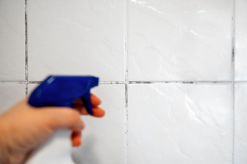 Woman applying a special anti fungal agent against black mould to the seams in bathroom, sealant, and wipes away dirt with a sponge. Home mold control concept. High quality photo