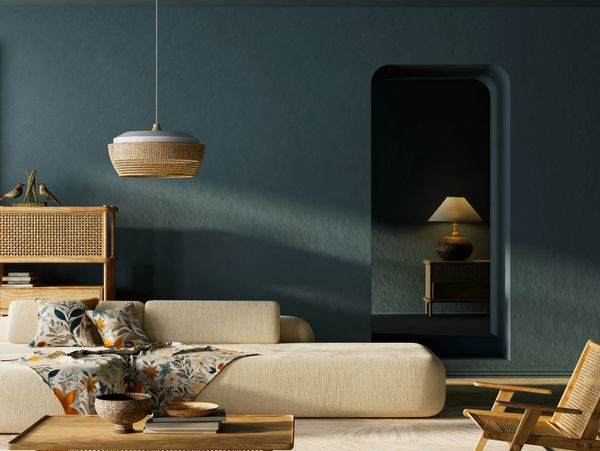 Cozy living room with beige sofa, floral throw, and wooden furniture against dark teal walls.