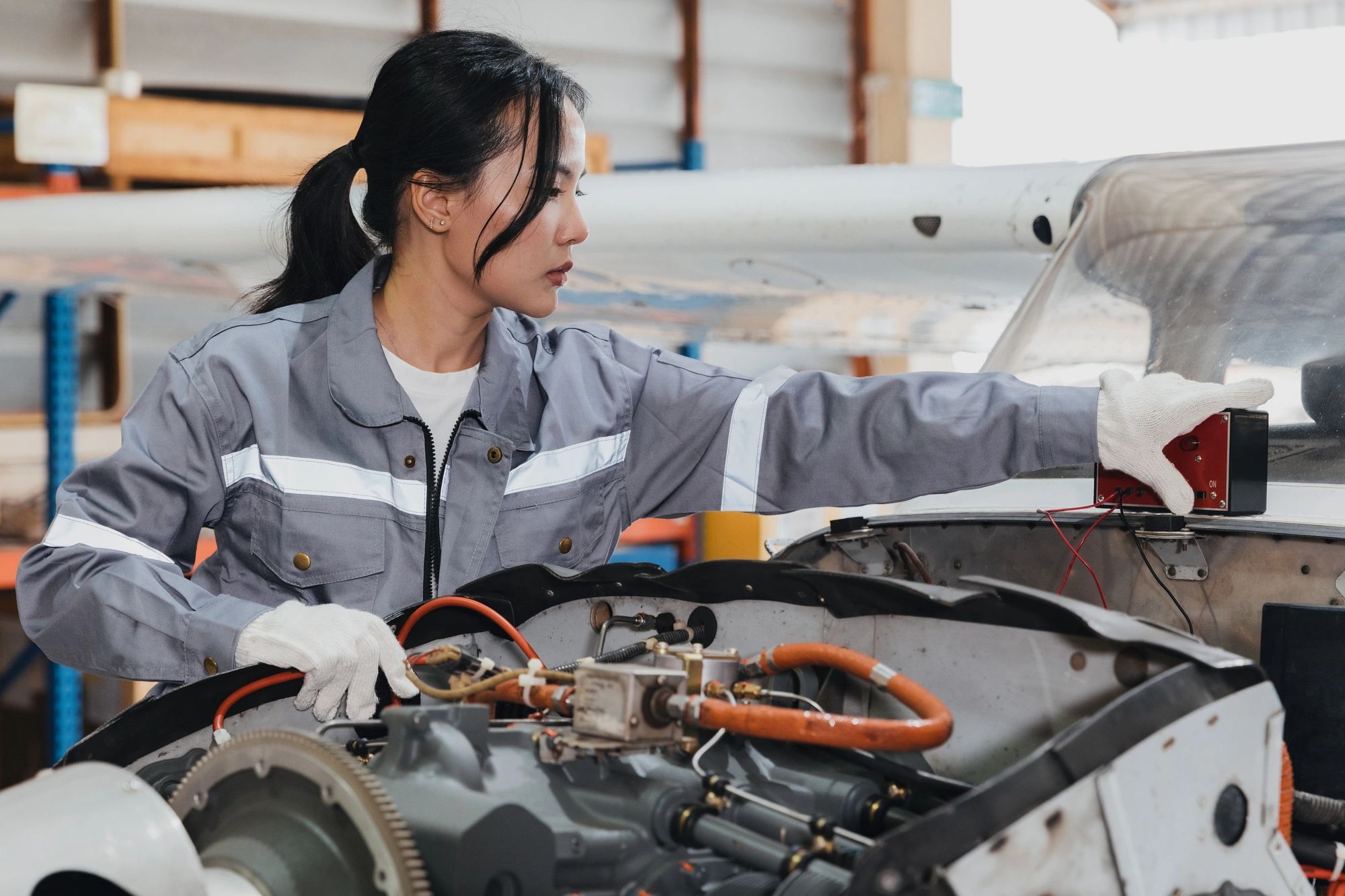 Woman inspecting aircraft engine with multimeter in hangar.