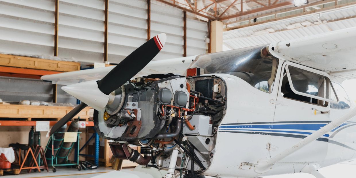 Small airplane engine with open hood in a hangar.