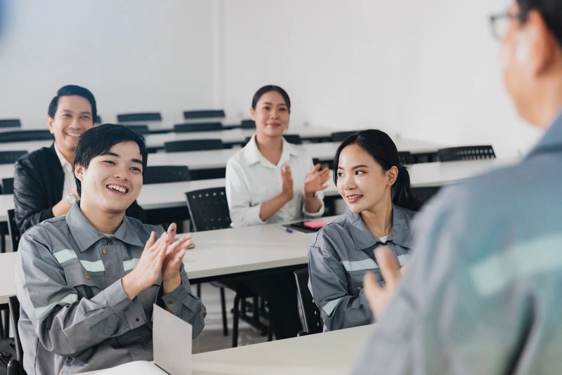 Employees engage in a training session, showing appreciation with applause. The setting is a modern classroom with attendees focused on the speaker.