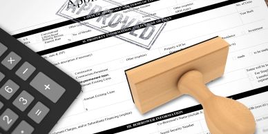 A loan application form stamped with 'APPROVED' next to a calculator and wooden stamp.