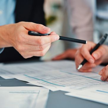 Two people reviewing and signing documents with pens in an office setting.