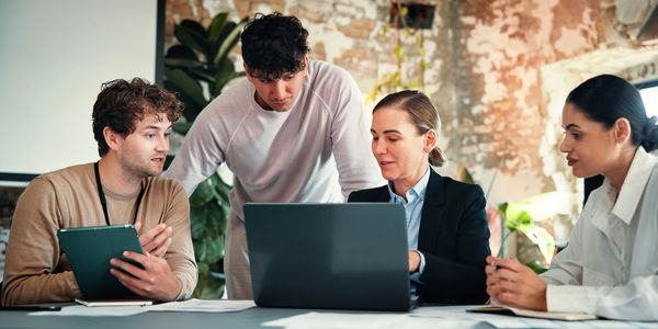 Four colleagues collaborating around a laptop in a modern office space.