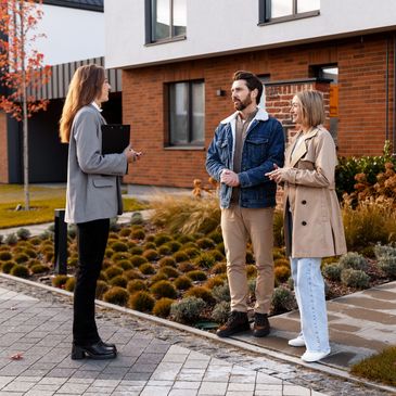 Couple talking to real estate agent outside house.