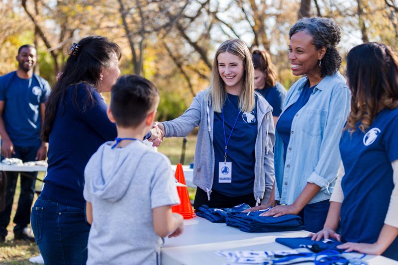 Volunteers at an outdoor event greet and interact with a child and other participants, distributing materials and spreading positive energy.