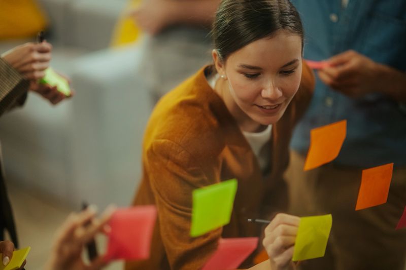 Young business team collaborating on project, writing notes on a glass board during a meeting, developing strategy and solutions