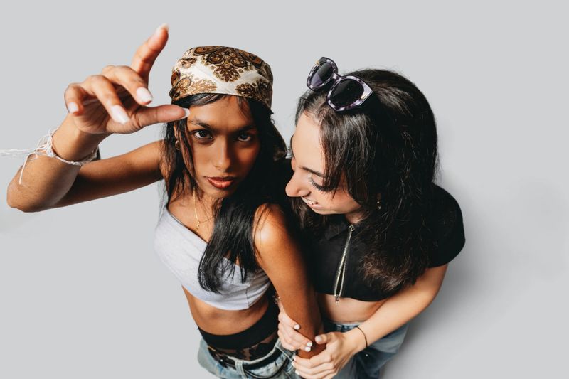 Two confident young women in Y2K street style pose in studio, bandana and sunglasses, showcasing friendship, diversity, and cool fashion trends