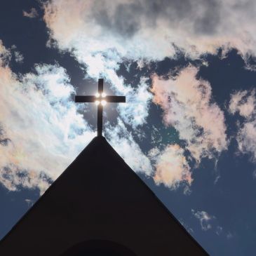 Silhouette of a cross against a partly cloudy sky.