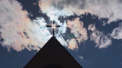 Sun shining through a cross on a church roof.