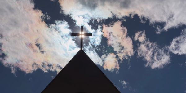 Sun shining through a cross on a church steeple.