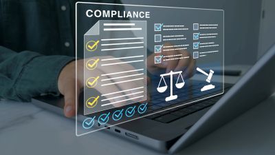 Person reviewing compliance checklist on a transparent digital interface above a laptop.