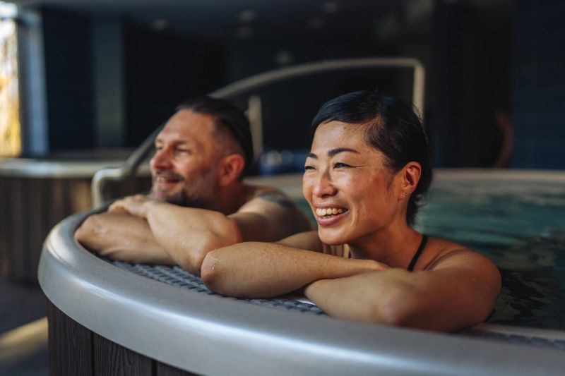 Happy smiling couple relaxing in a warm hot tub at a luxury wellness resort, leaning on the spa edge and enjoying tranquil hydrotherapy, bonding and carefree vacation joy