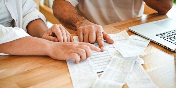 Two people reviewing receipts and documents on a wooden table beside a laptop.