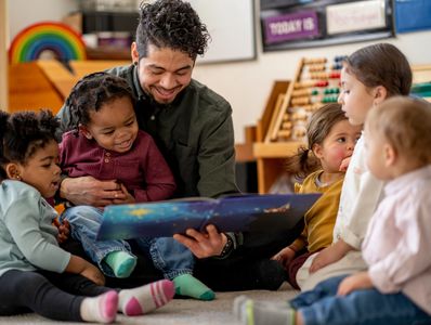A man reads a book to a group of young children in a classroom setting.