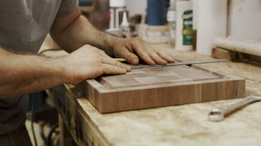 Craftsman sanding a wooden board in a workshop.