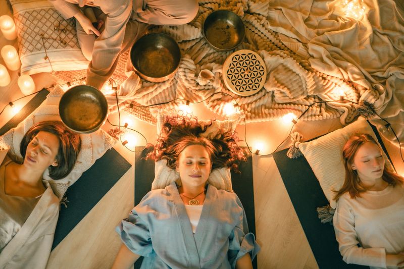 A calming group sound healing session with three people lying in relaxation as Tibetan bowls and warm lights create a soothing wellness atmosphere ideal for meditation, stress relief, mindfulness, and holistic healing.