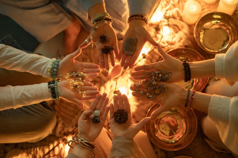 A group meditation scene with people holding crystals, beads, pinecones and symbolic objects in their hands. Warm candlelight and singing bowls create a peaceful, spiritual atmosphere for mindfulness and connection.