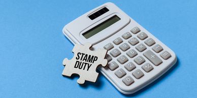 A calculator with a puzzle piece leaning on it. On the puzzle piece is written 'stamp duty'.