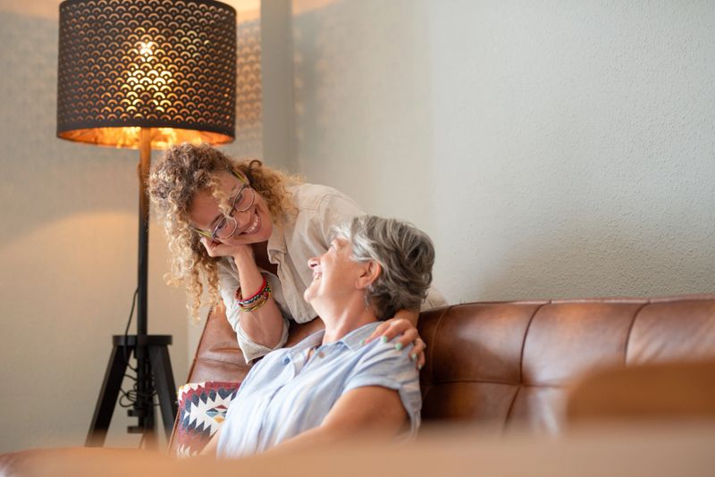Portrait of happy mature blonde woman hugging her elderly mother sitting on sofa. The scene captures tenderness, affection, emotional connection, symbolizing love, care, companionship in later life