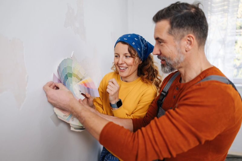 A couple joyfully selecting color palettes for painting their wall, showcasing enthusiasm and collaboration in home improvement and personal expression through colors.