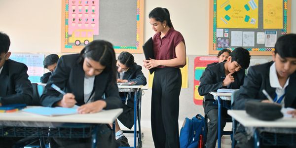 Teacher supervising students writing in classroom during exam.